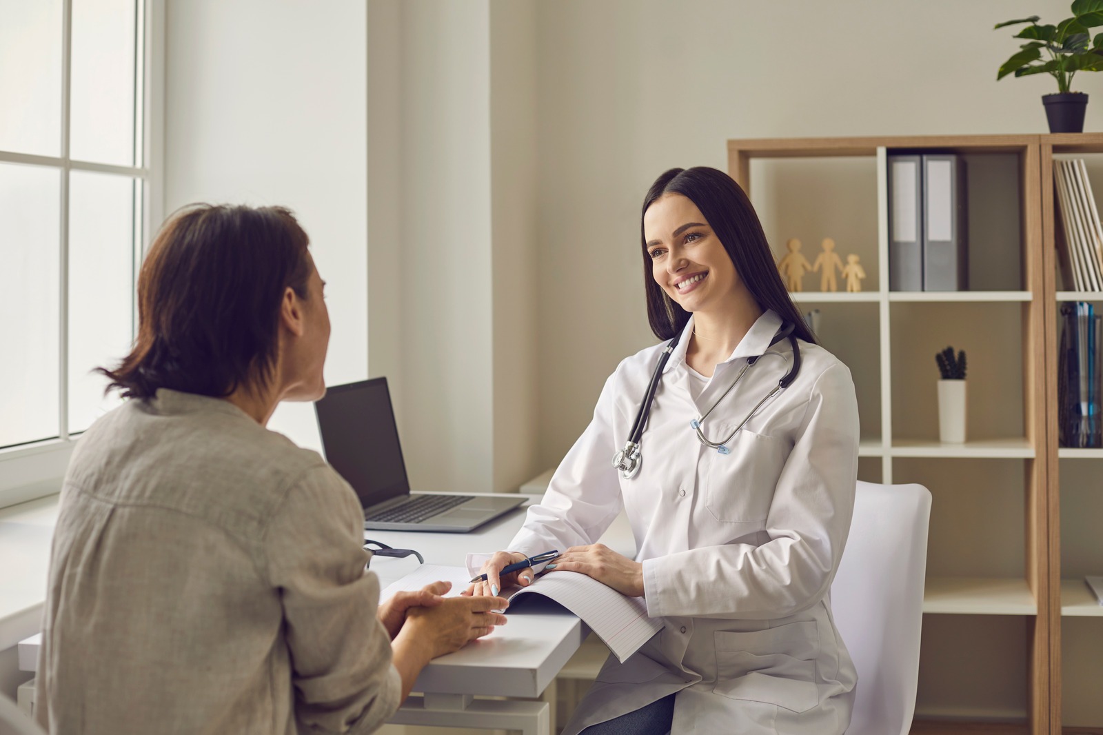 Smiling doctor therapist listening to complaints of woman patient during visit in medical clinic